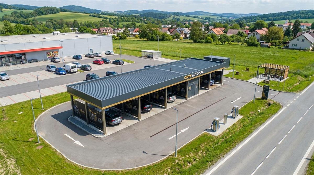 Letecký pohled na mycí centrum ONYX s jednosměrným průjezdem, vysavači a pergolou, vedle parkoviště supermarketu